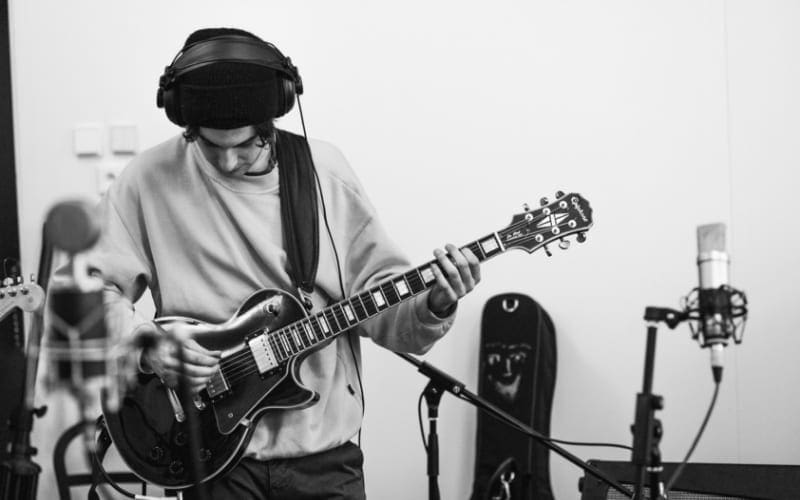 musician playing guitar whilst recording in studio