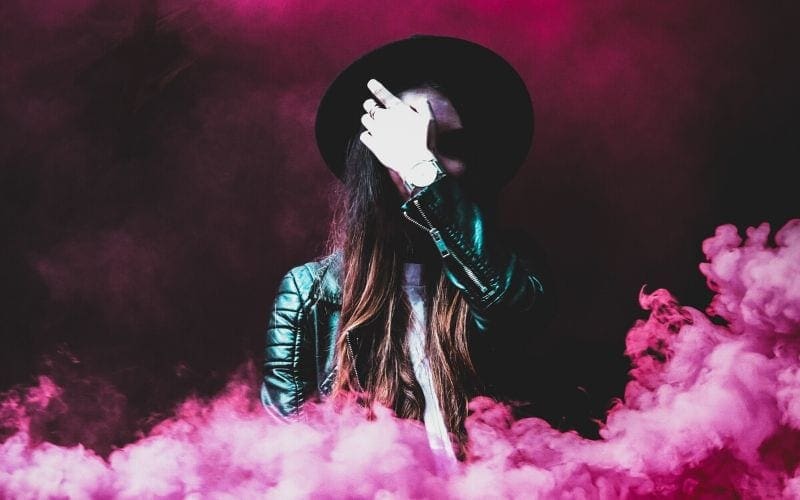 musician wearing hat in pink cloud of smoke