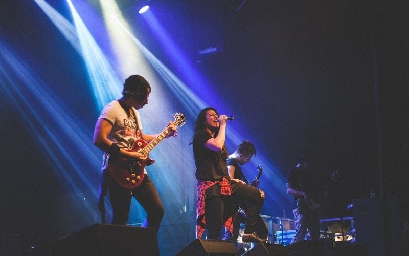 Band on stage in blue light finding artists is essential to starting a record label